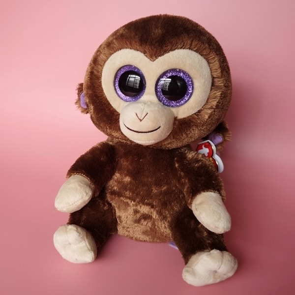 Peluche pequeño de mono marrón sobre fondo rosa