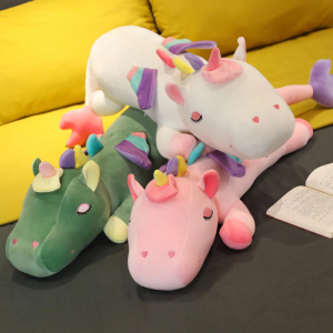 3 grandes peluches de unicornio, los dos de abajo son verde y rosa y el de arriba es blanco, se ve un sofá amarillo al fondo y están colocados sobre un suelo negro